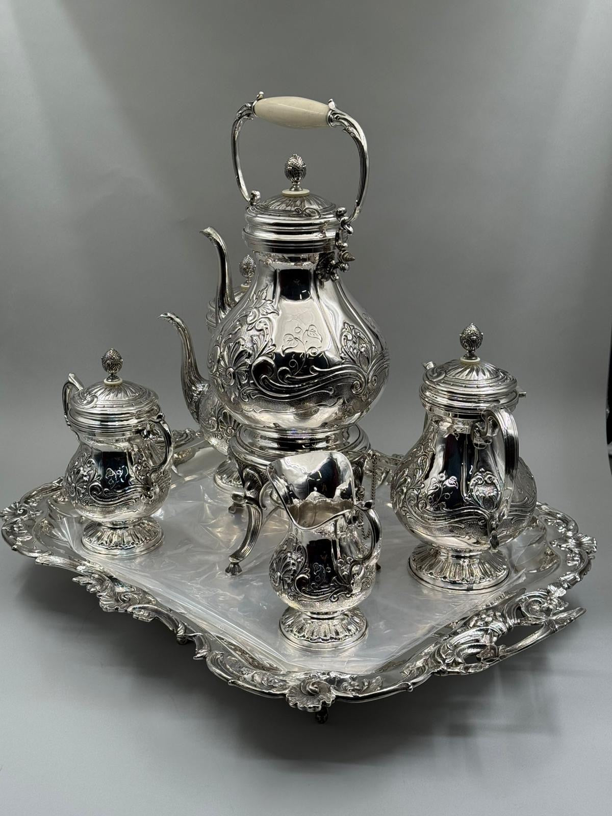 Silver tea set with a teapot, creamer, sugar bowl, and tray on a gray background